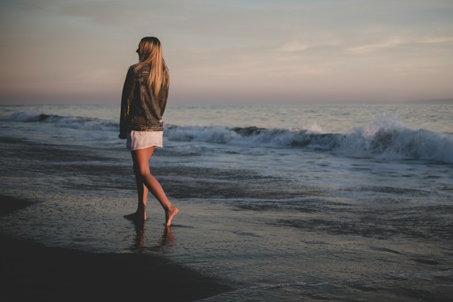 Vrouw loopt blootsvoets door de branding bij zonsondergang